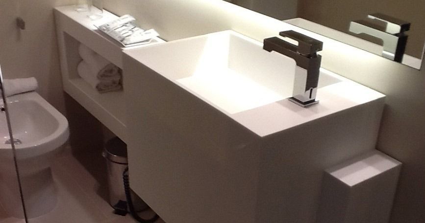 Lavabo moderno de color blanco con grifo cromado, espejo y inodoro visibles junto al tocador.