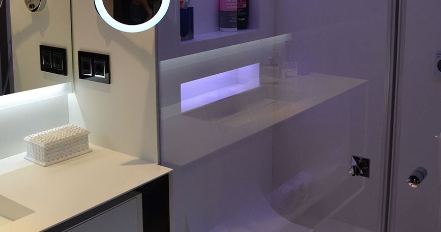 Interior de laboratorio moderno con mostradores blancos, panel de pared iluminado y un pequeño estante con muestras a la izquierda.
