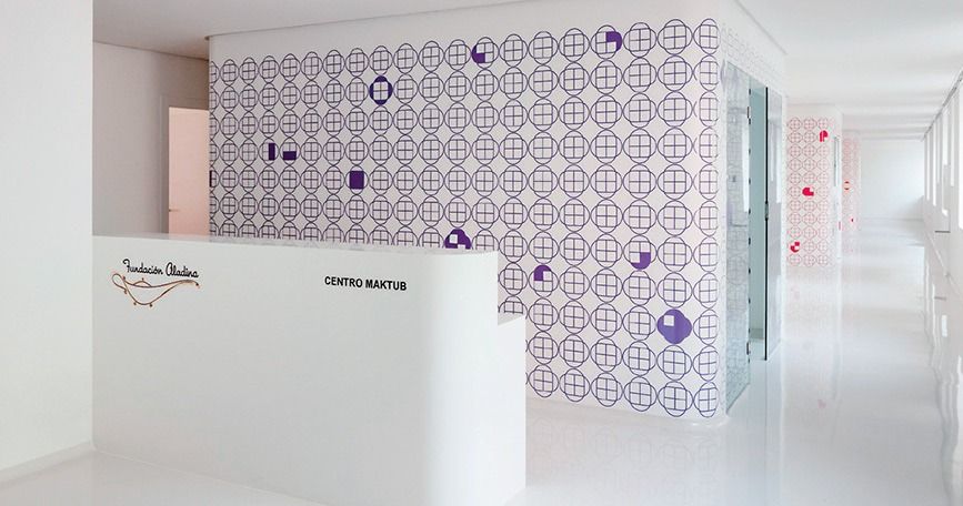 Pasillo blanco luminoso con pared estampada en color púrpura y mostrador de recepción en un interior moderno.