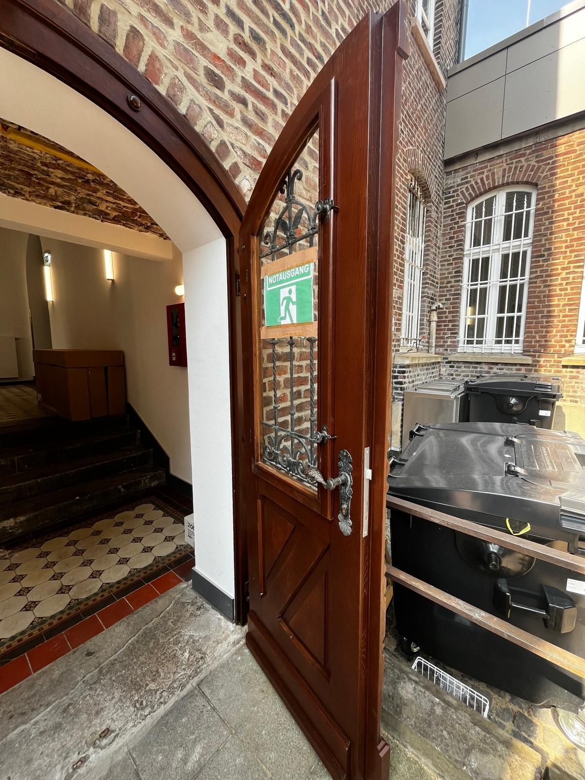 Eingangstür mit Rundung im Vintagestil mit verschnörkelten Eisenbeschlägen und -gittern vor den Fenstern