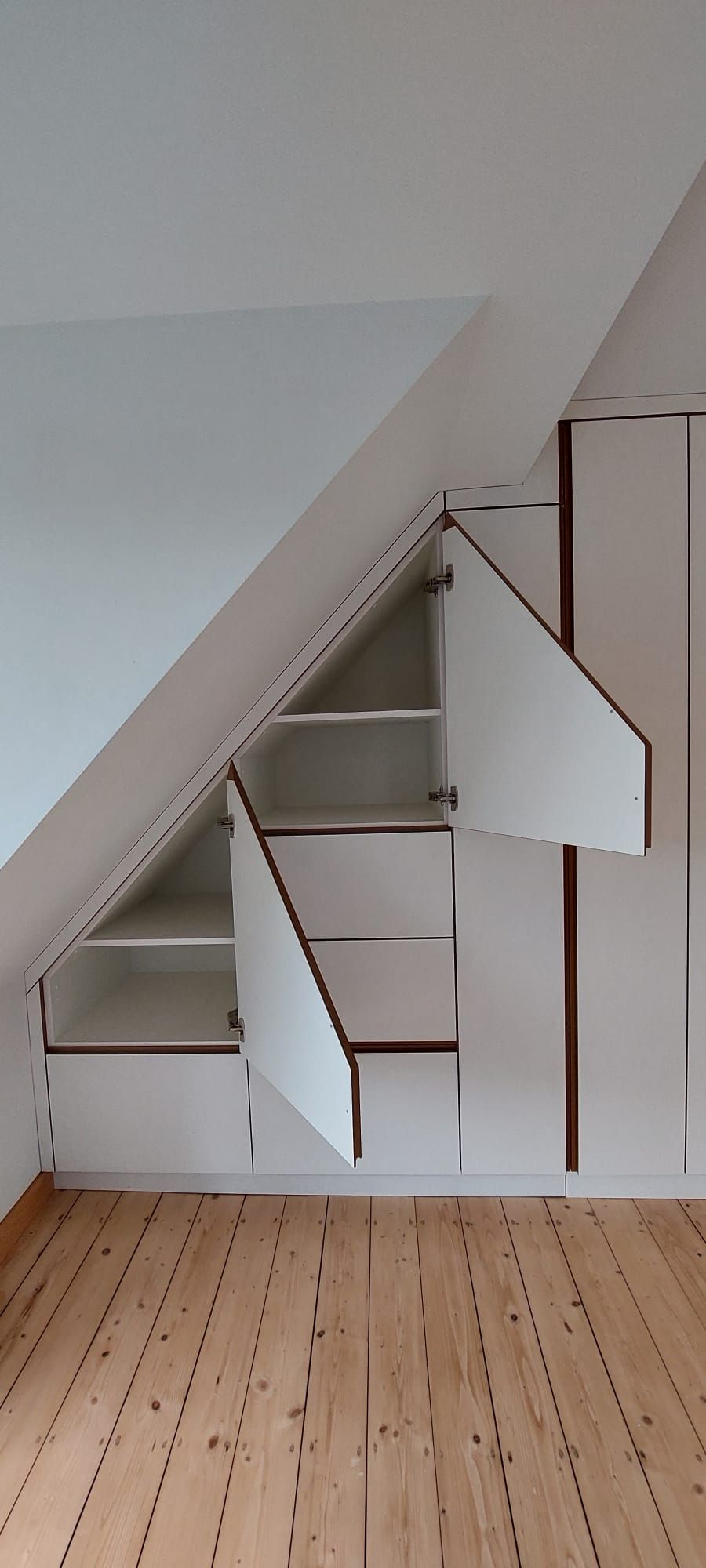 Weißer Einbauschrank im Schlafzimmer mit geöffneten Schranktüren in der Schräge