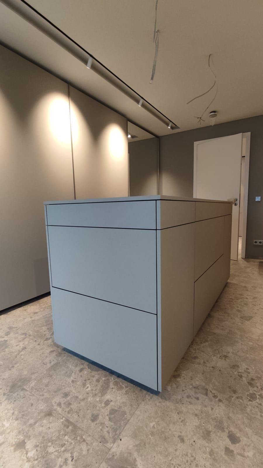 In der Mitte des Raumes befindet sich eine große Schrankinsel mit vielen geschlossenen Schubfächern.