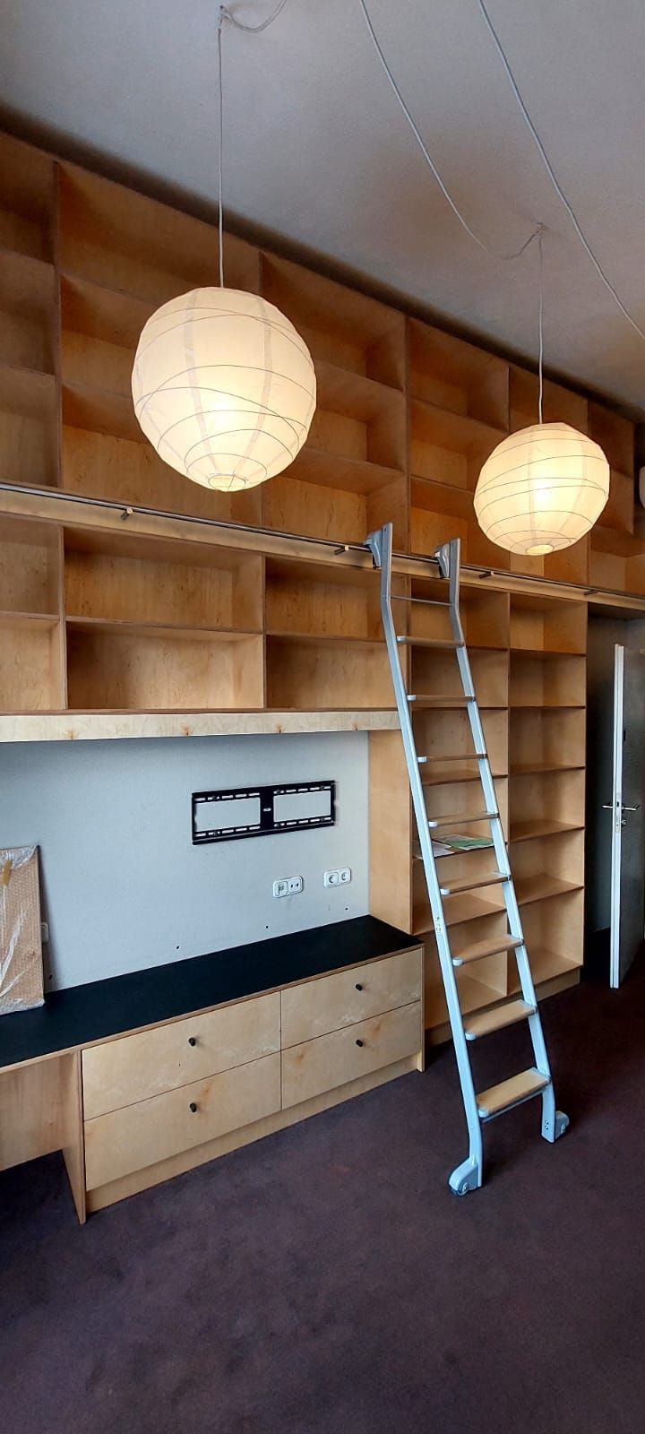 Eine große Schrankwand im Aufbau mit integrierter Schiene und Leiter daran