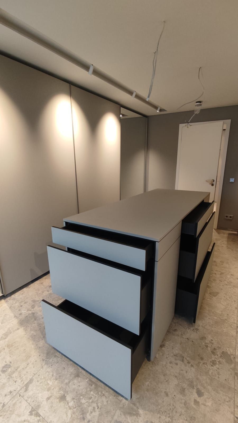 In der Mitte des Raumes befindet sich eine große Schrankinsel mit vielen geöffneten Schubfächern.