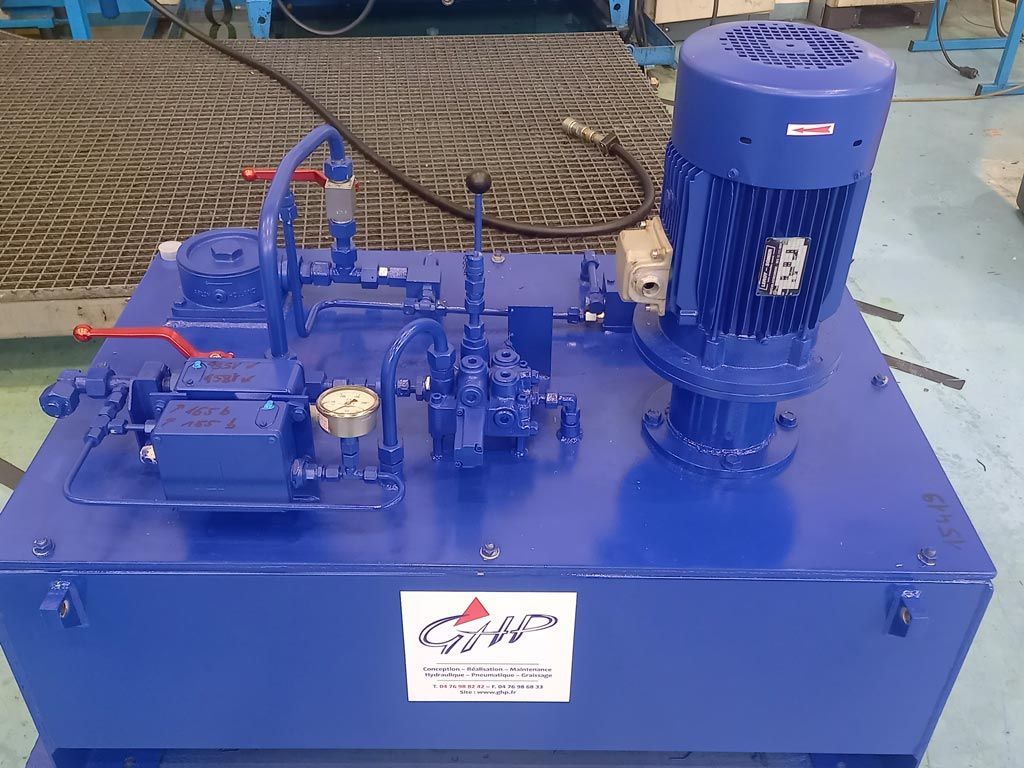 Groupe hydraulique industriel bleu avec moteur électrique, monté sur un réservoir dans un atelier.