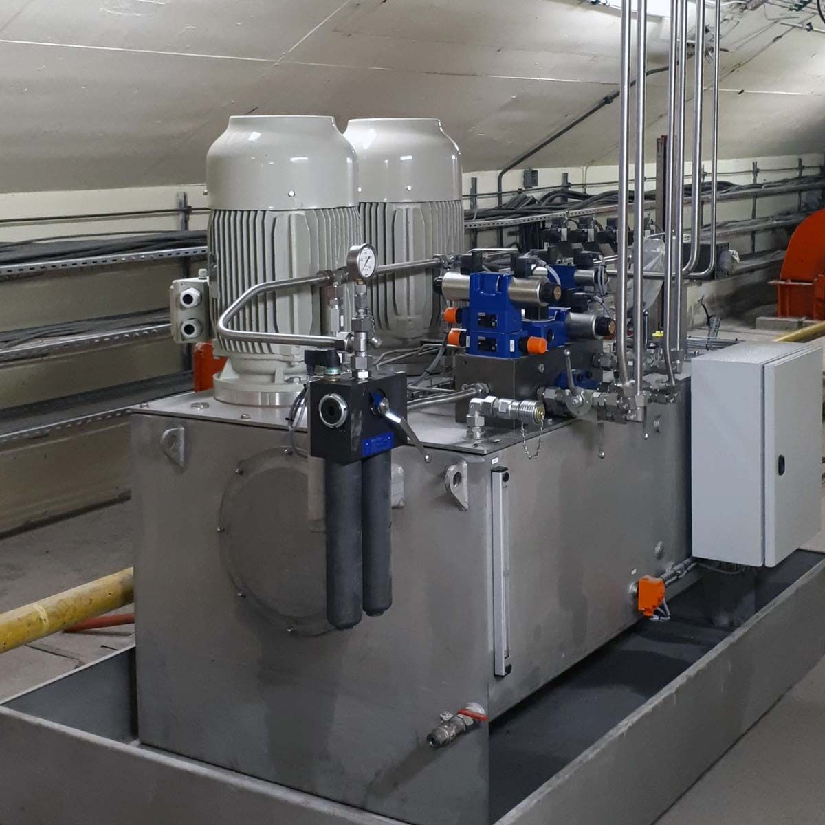 Un groupe hydraulique en acier inoxydable avec deux moteurs et des vannes de régulation dans un local technique industriel.