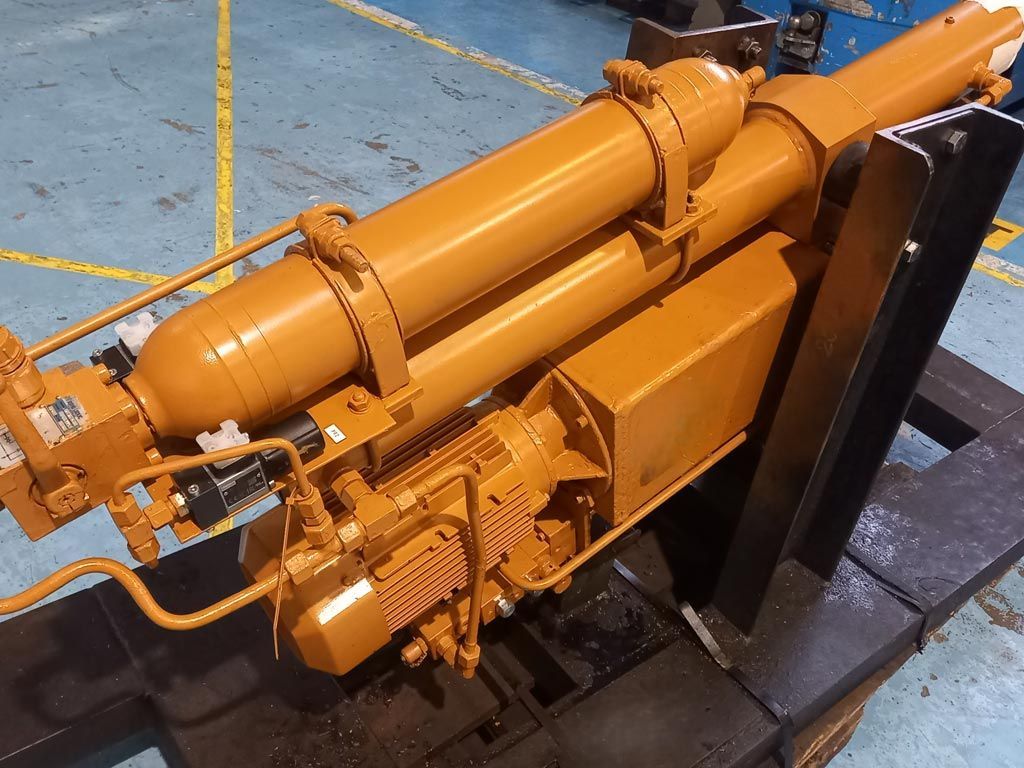 Groupe hydraulique industriel jaune avec réservoir cylindrique et tuyauterie métallique, monté sur un support dans un atelier.
