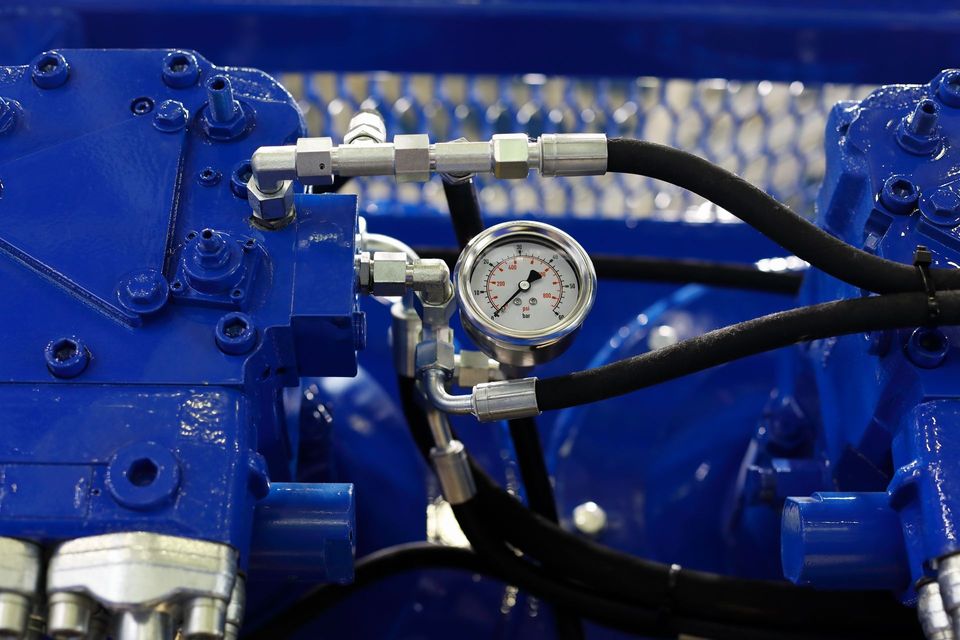 Gros plan sur une machine bleue avec un manomètre et des tuyaux noirs.