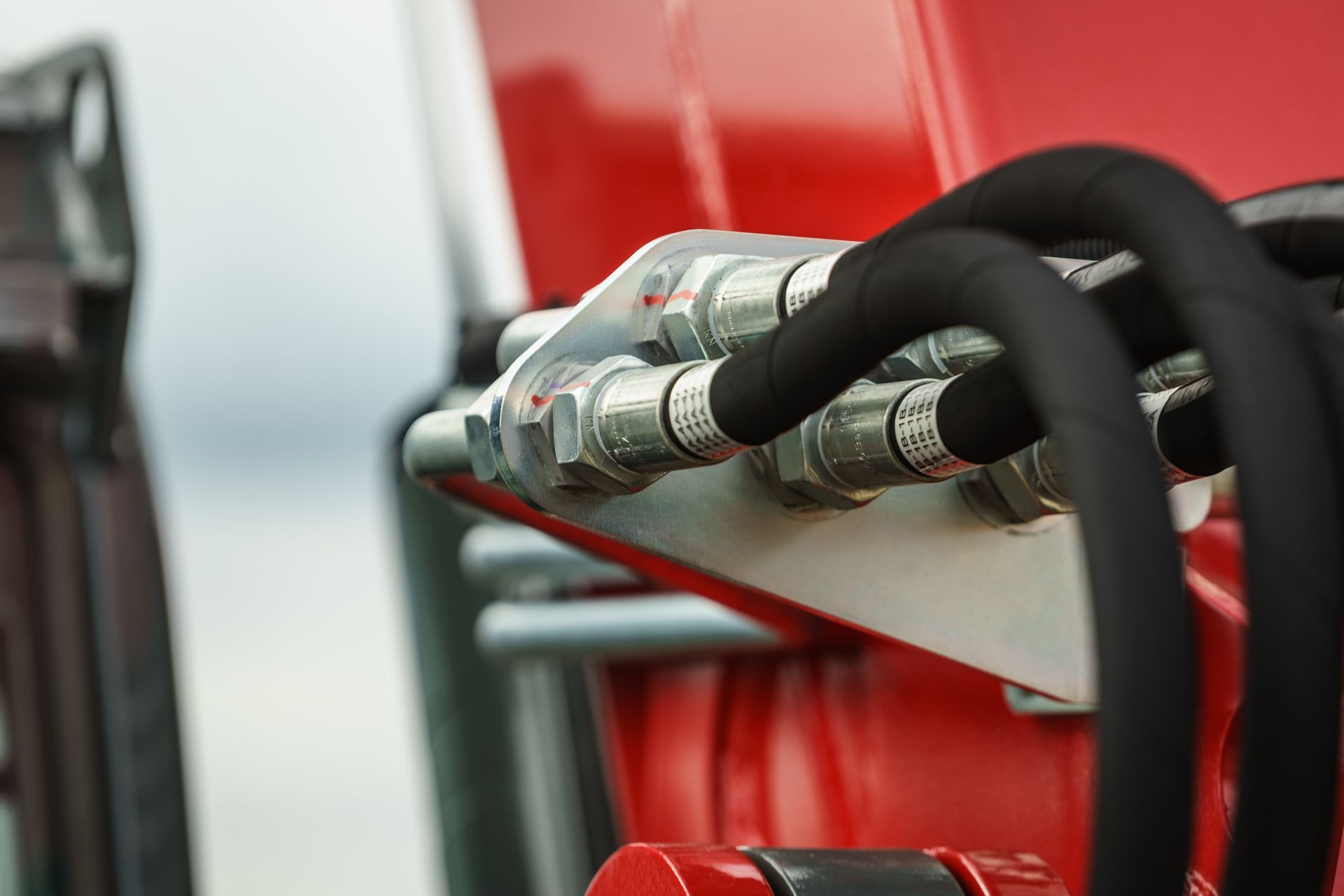 Gros plan sur une machinerie rouge avec des raccords hydrauliques argentés et des tuyaux noirs.