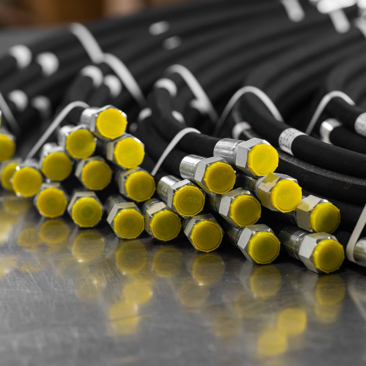 Des faisceaux de tuyaux hydrauliques noirs avec des bouchons jaunes, sur une surface métallique.