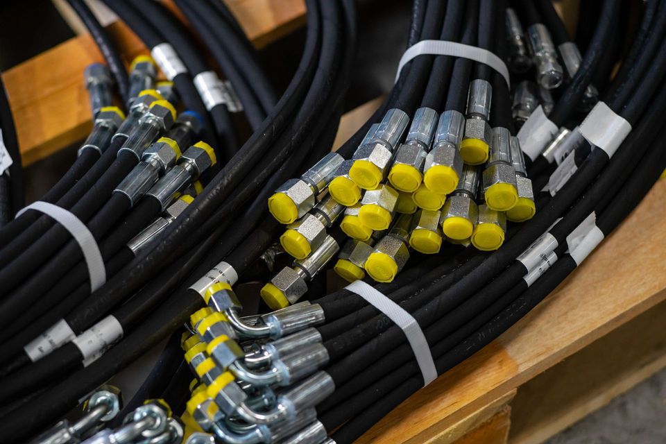 Faisceaux de flexibles hydrauliques noirs avec raccords métalliques et capuchons de protection jaunes.