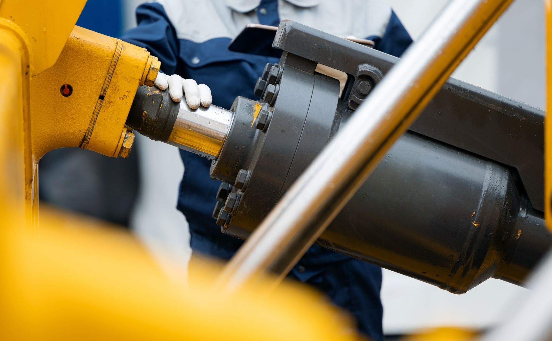 Personne en uniforme de travail raccordant un composant mécanique noir à une machine jaune.