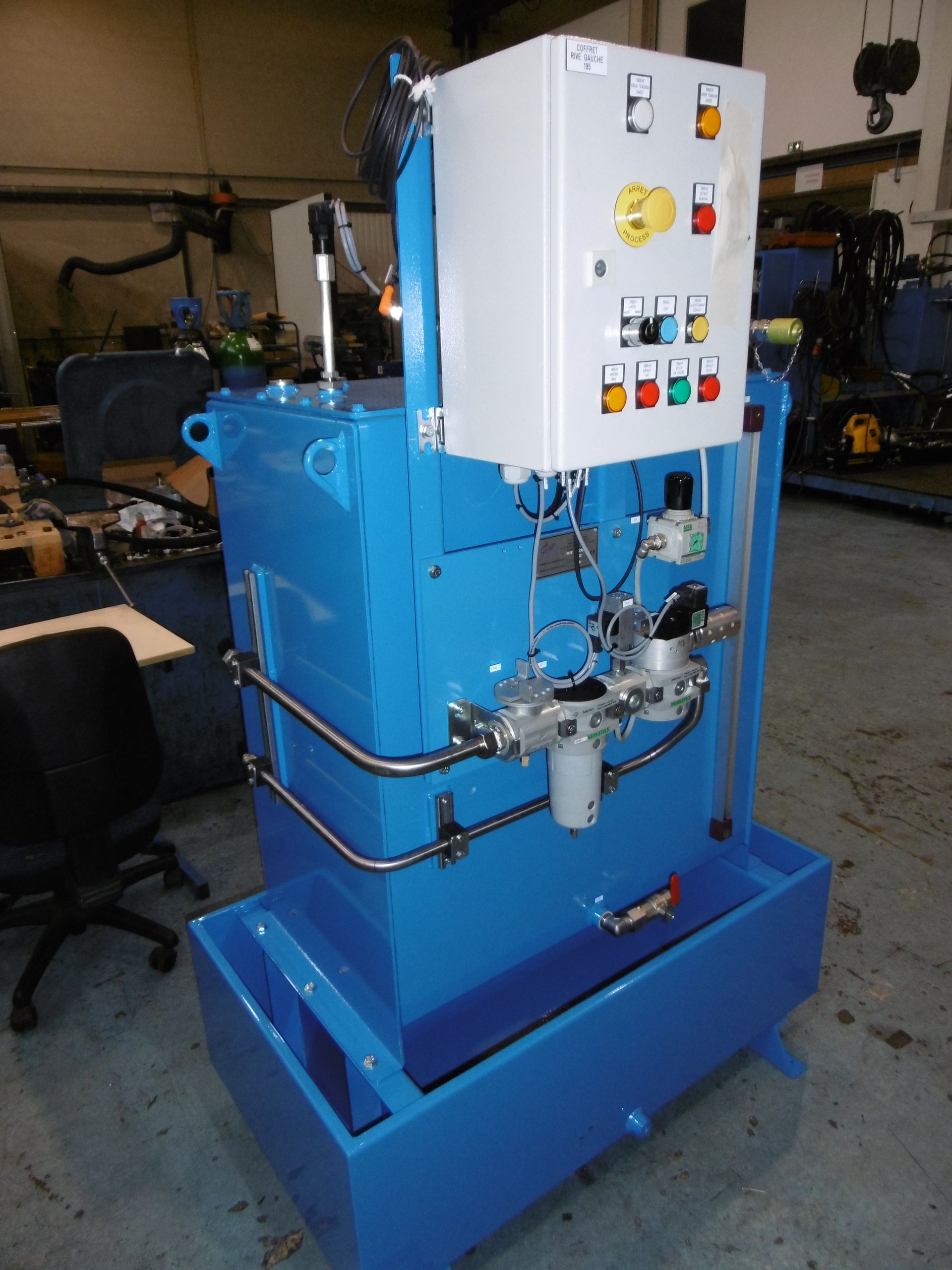 Une centrale hydraulique industrielle bleu vif, équipée d'un boîtier de commande et de filtres, est installée dans un entrepôt.