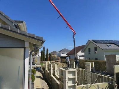 Eine Betonpumpe füllt an einem sonnigen Tag Beton in die Schalung einer Hauswand auf einer Wohnbaustelle.