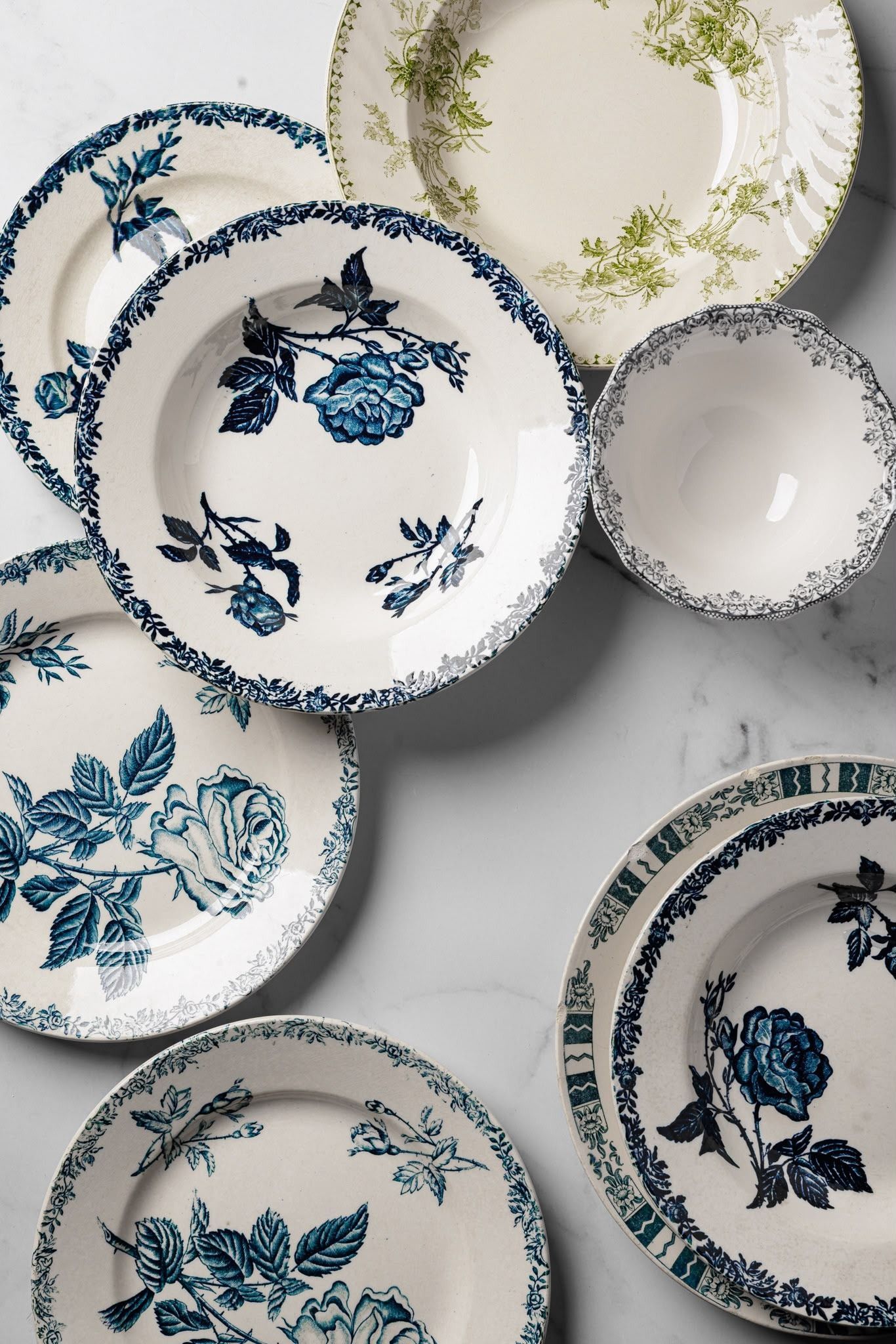 Platos florales vintage apilados en azul, verde y gris sobre un fondo claro