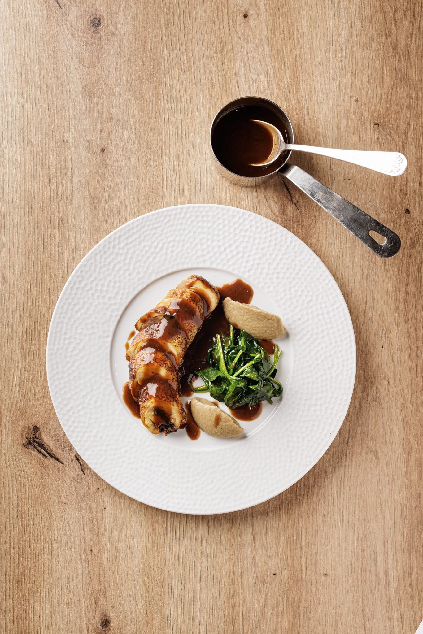 Pollo asado emplatado con verduras sobre una mesa de madera, junto a una taza de café y una cuchara
