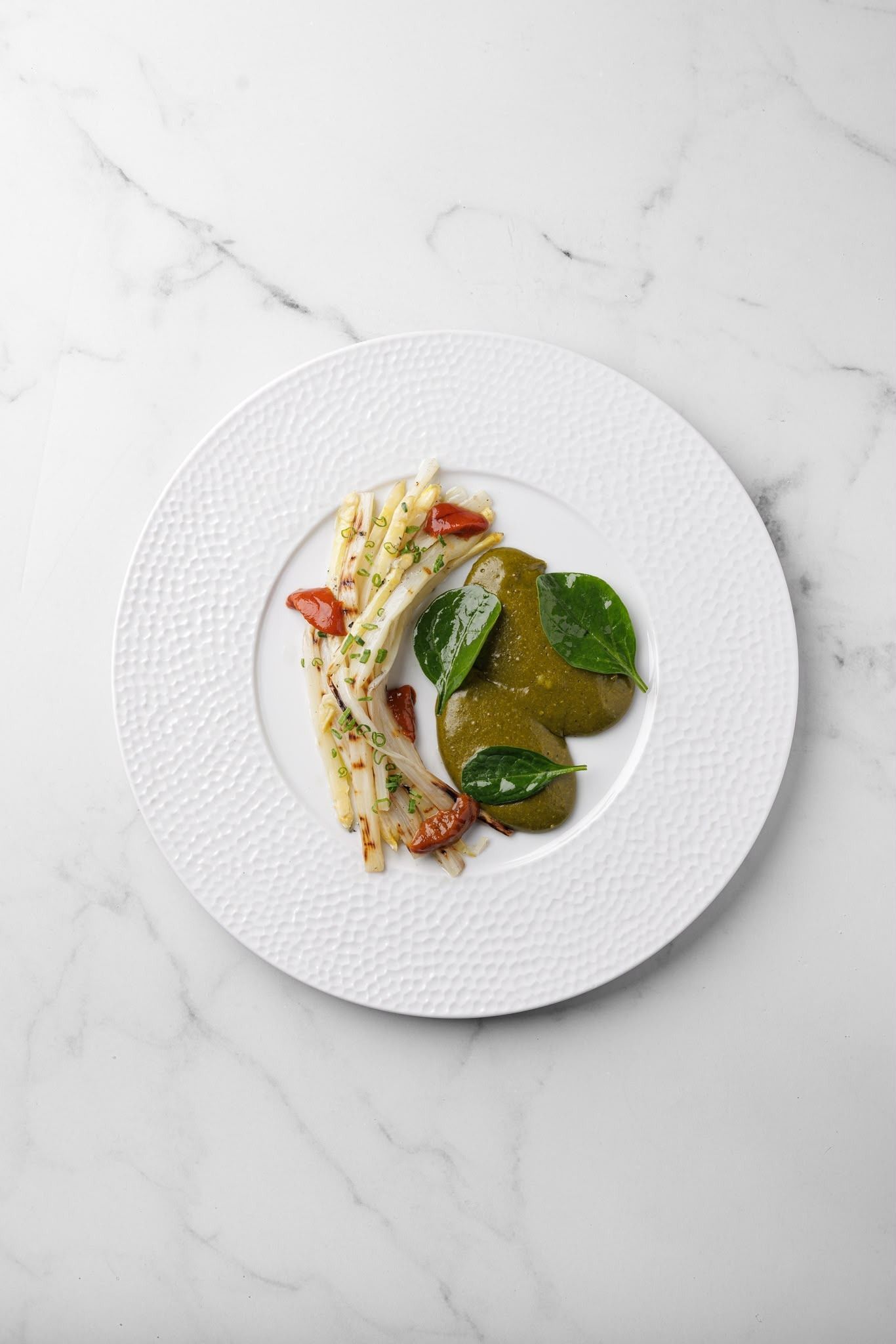 Plato gourmet de pescado con verduras verdes y guarnición roja sobre una mesa de mármol blanco