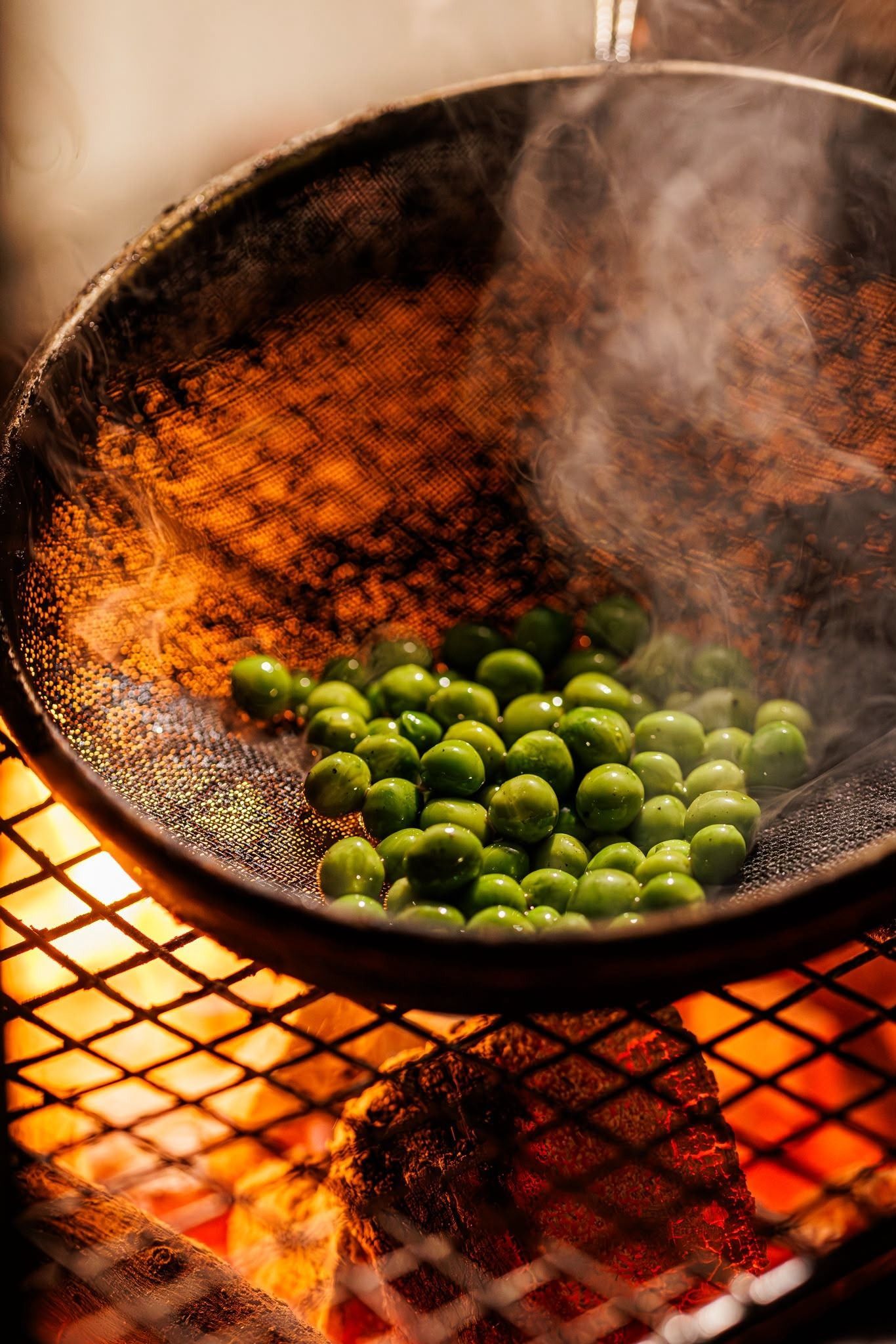 Guisantes verdes chisporroteando en un wok negro sobre una llama viva, con vapor elevándose sobre una parrilla metálica.