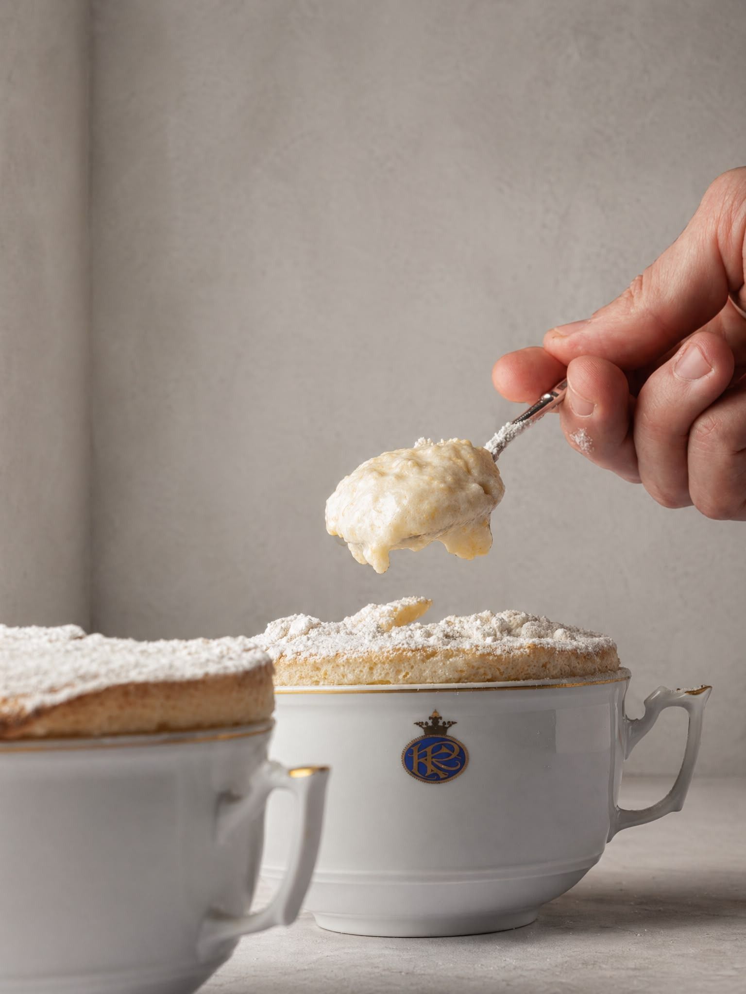 Una mano coloca una cucharada de nata montada sobre un postre en una taza de té blanca
