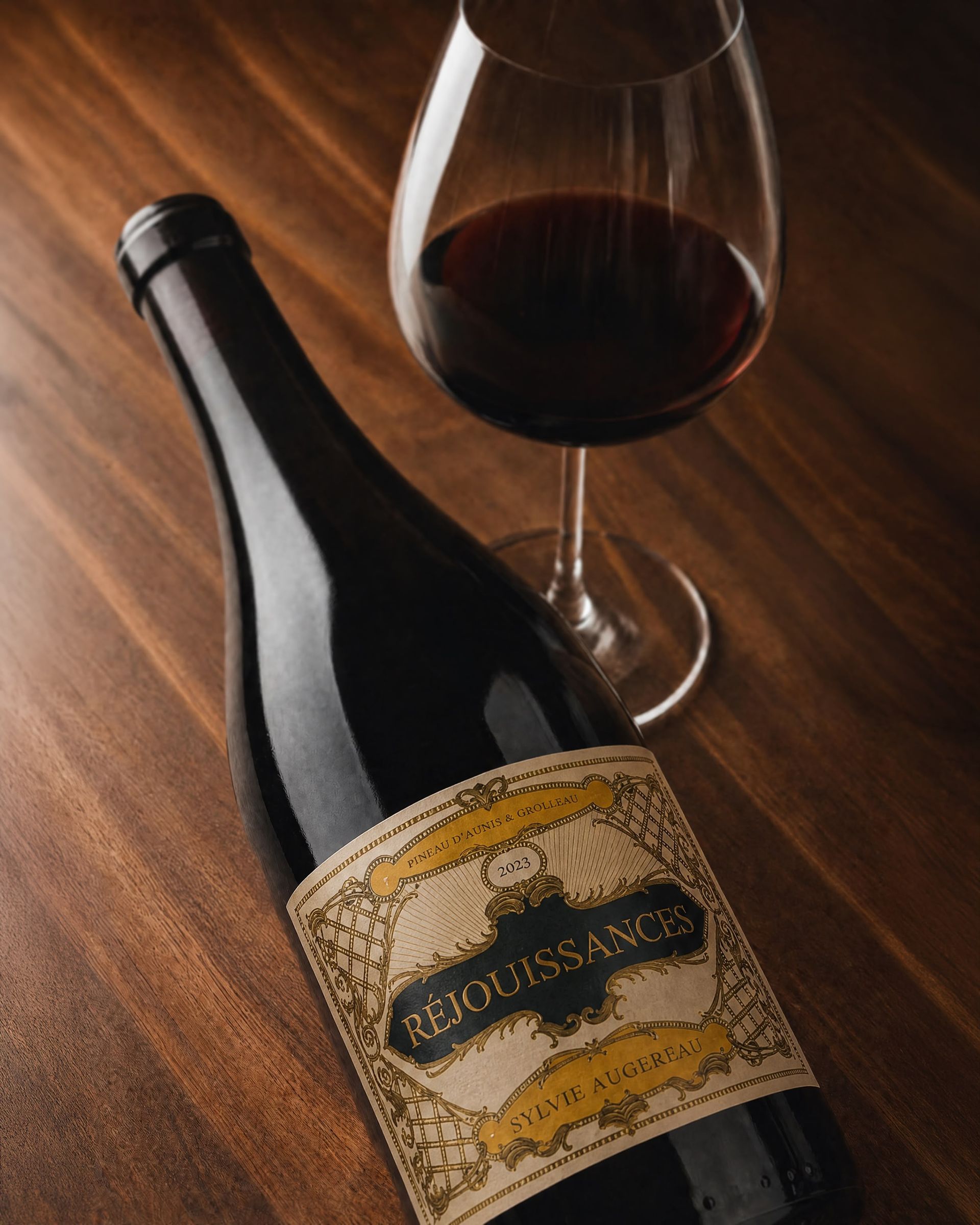 Una botella de vino tinto junto a una copa llena de vino sobre una mesa de madera.