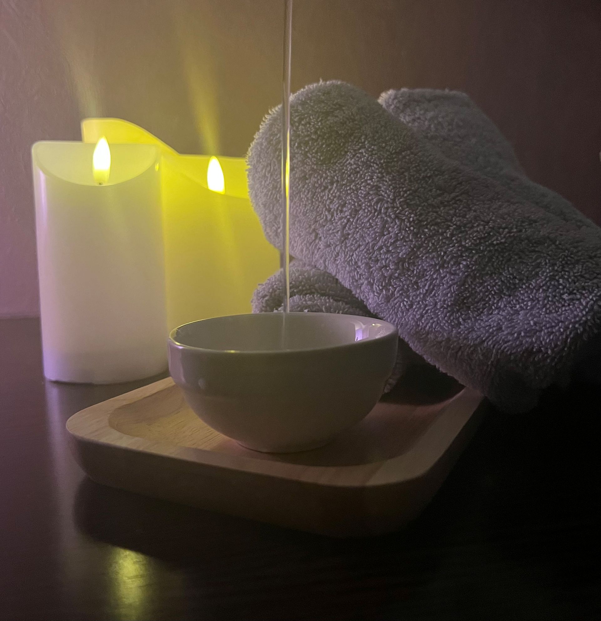 Ambiance spa avec des bougies allumées, un bol et des serviettes pliées sur un plateau, dans une lumière tamisée