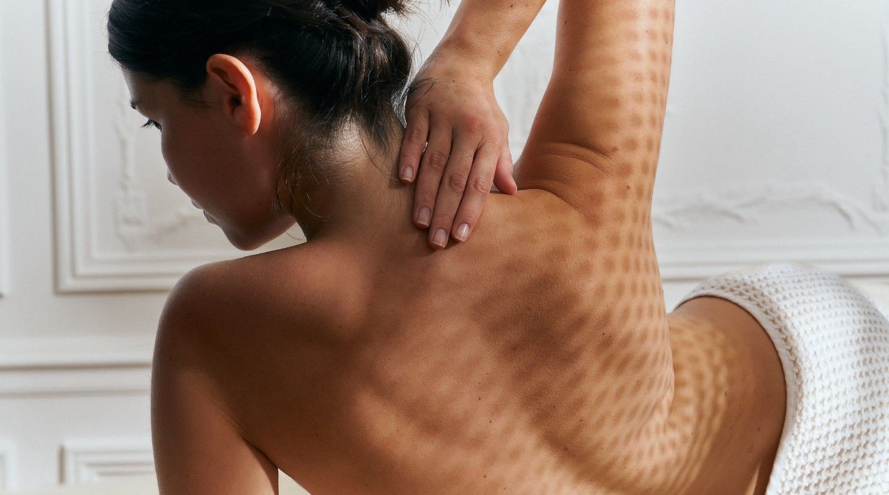 Personne recevant un massage du dos sur un lit blanc, avec des mains appuyant sur le haut du dos et la nuque
