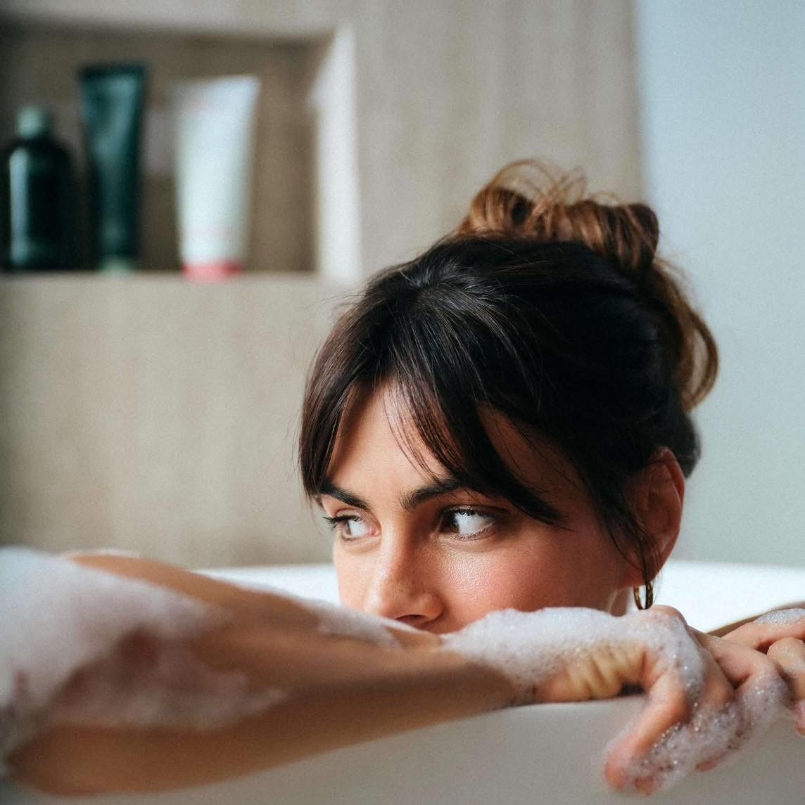 Femme se relaxant dans un bain moussant, regardant par-dessus le bord de la baignoire, les bras posés dessus