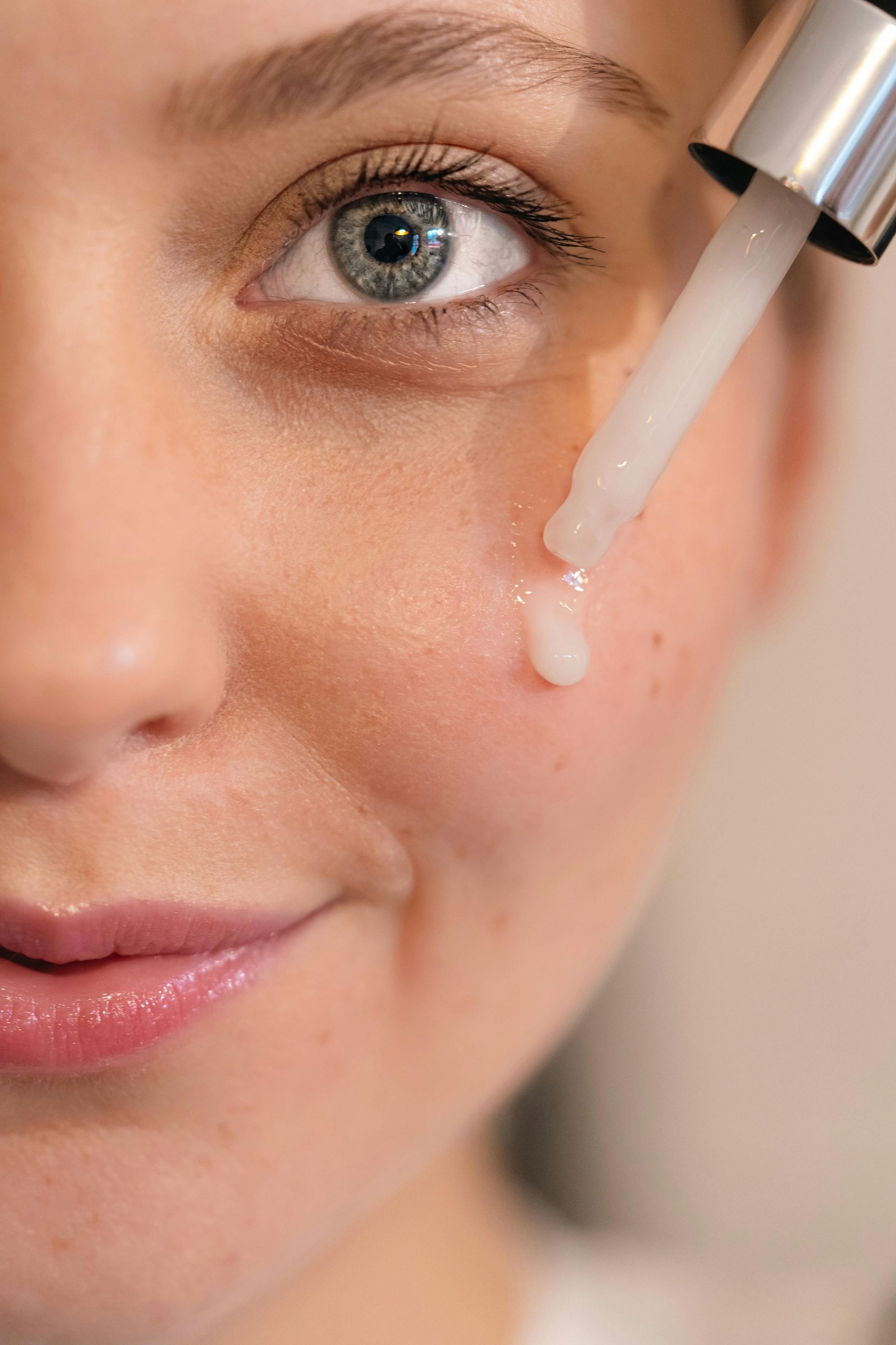 Gros plan sur une femme qui applique une goutte de sérum transparent sur sa joue à l’aide d’une pipette.