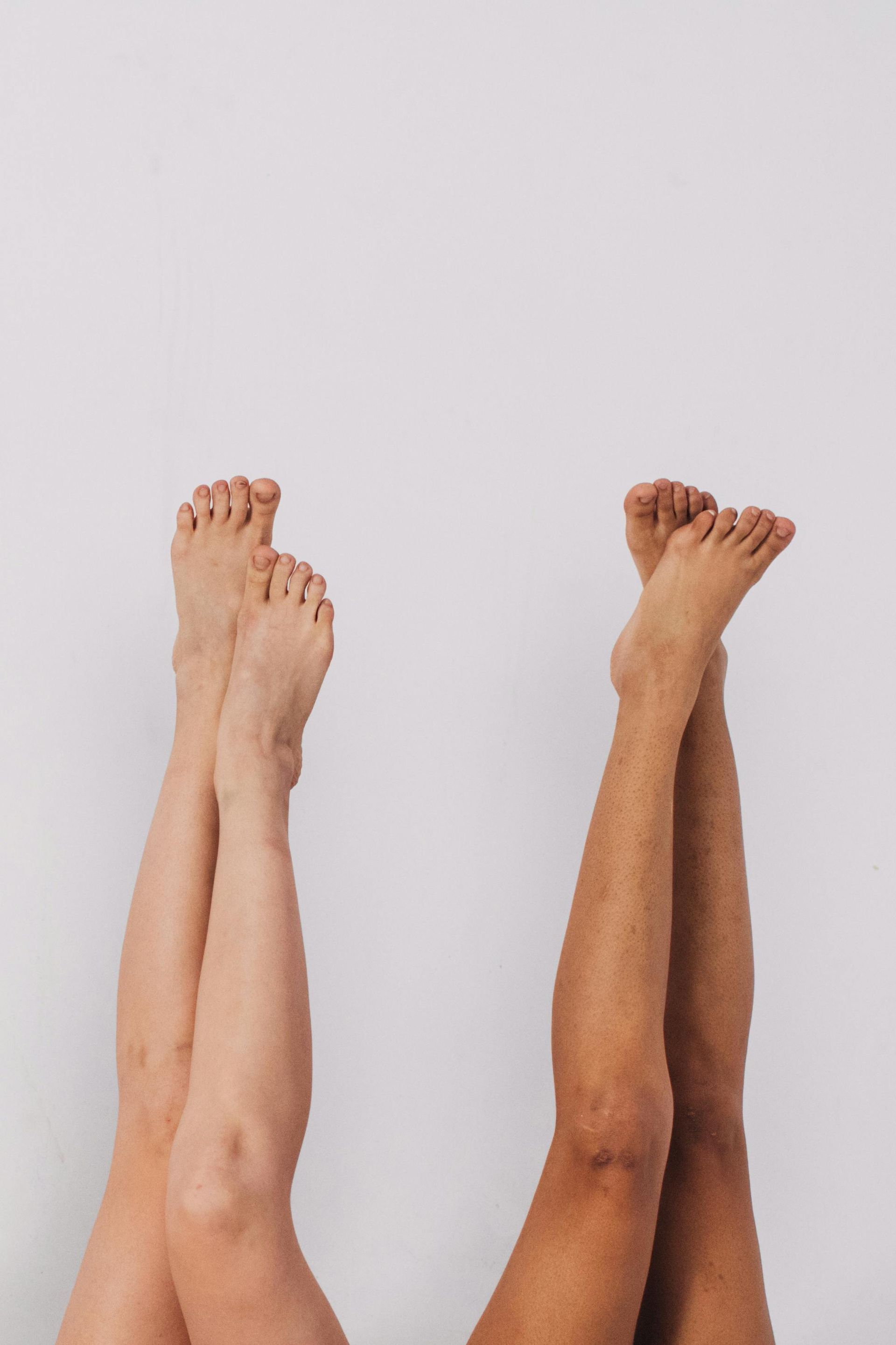 Deux paires de jambes et de pieds levés sur un fond clair uni