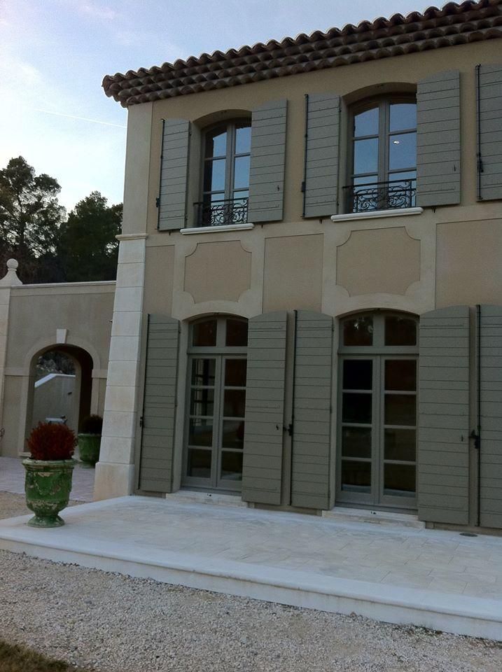 Bâtiment en stuc beige avec volets et fenêtres gris, toit en tuiles de terre cuite et entrée cintrée.