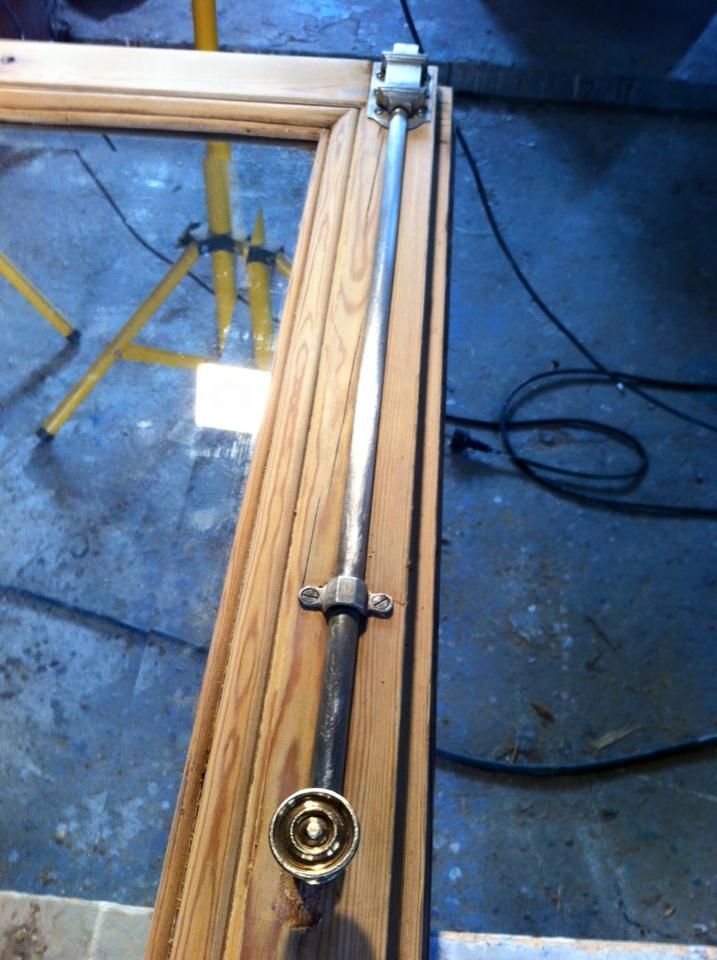 Un long verrou métallique sur un cadre en bois, probablement un élément de fenêtre.