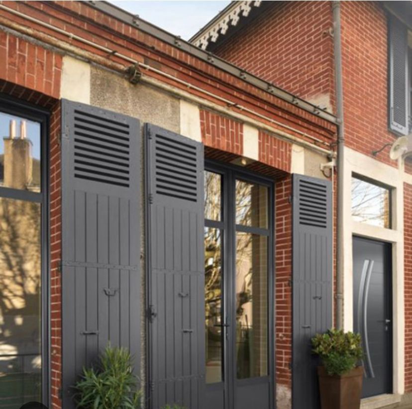 Volets gris sur un bâtiment en briques avec de grandes portes vitrées.