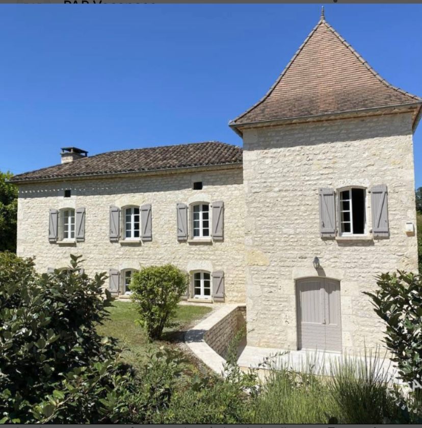Maison en pierre aux volets gris et à la tour, sous un ciel d'un bleu limpide.