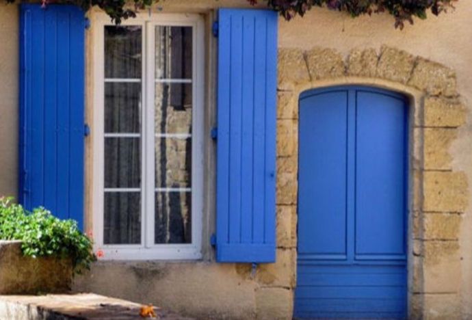 Fenêtre blanche à volets bleus à côté d'une porte bleue sur un bâtiment en pierre.
