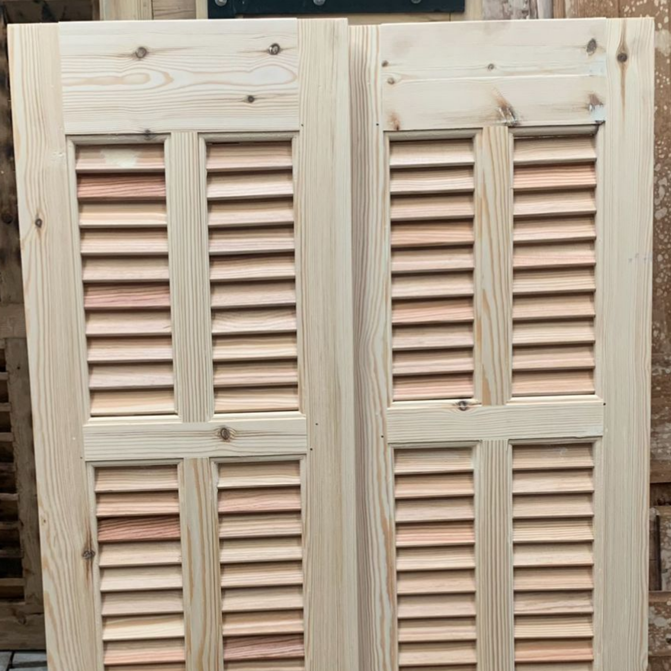 Deux panneaux de volets en bois brut, à lattes horizontales.