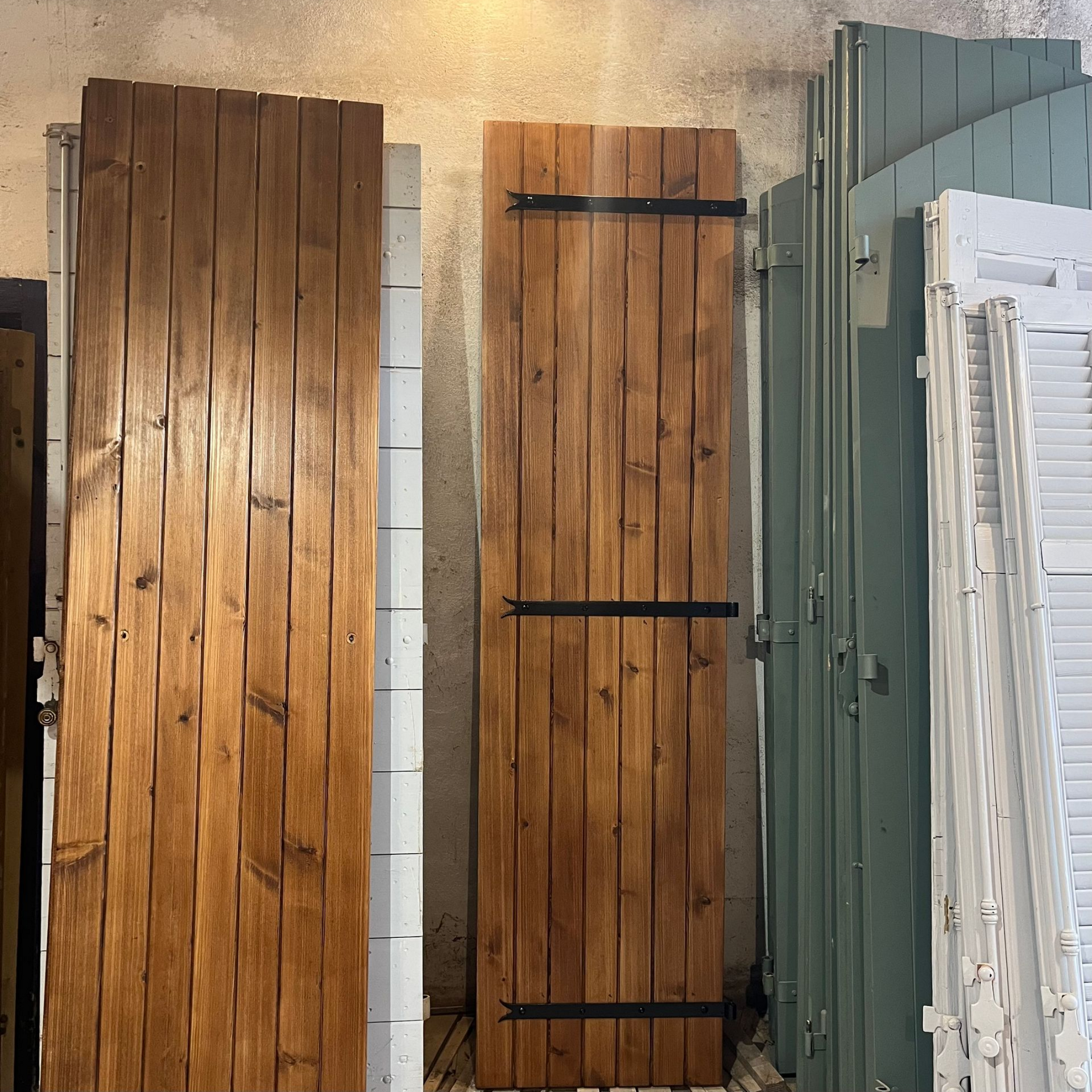 Deux volets en bois avec des ferrures sombres, appuyées contre d'autres volets.