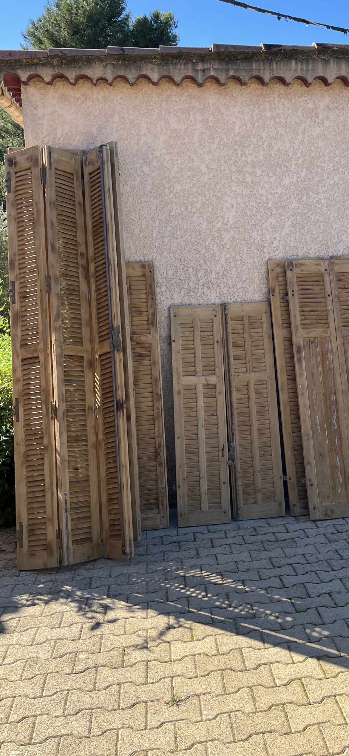 Des volets en bois sont appuyés contre un mur en stuc, posé sur une surface pavée de briques.