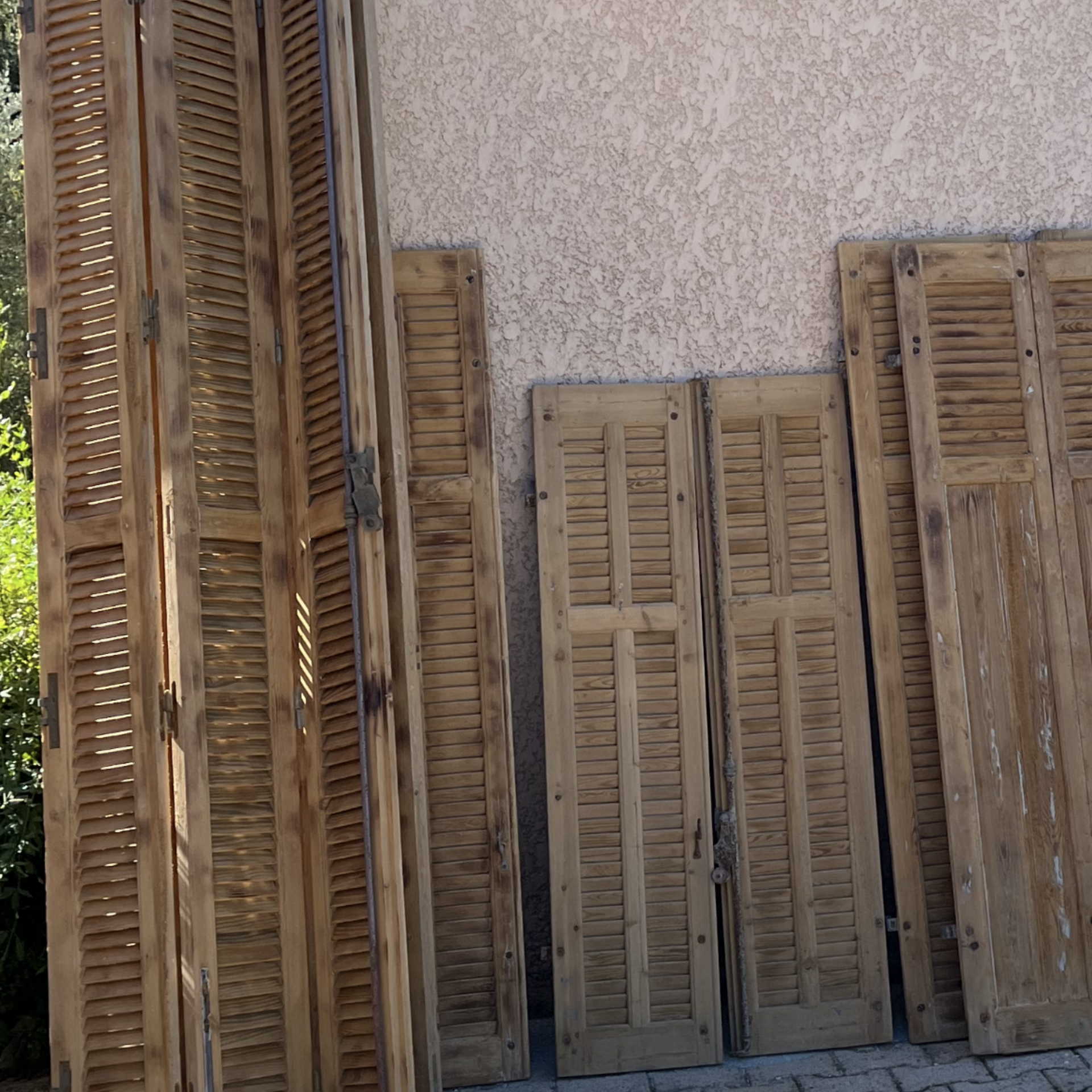 Des volets en bois de tailles différentes sont appuyés contre un mur en stuc à l'extérieur.