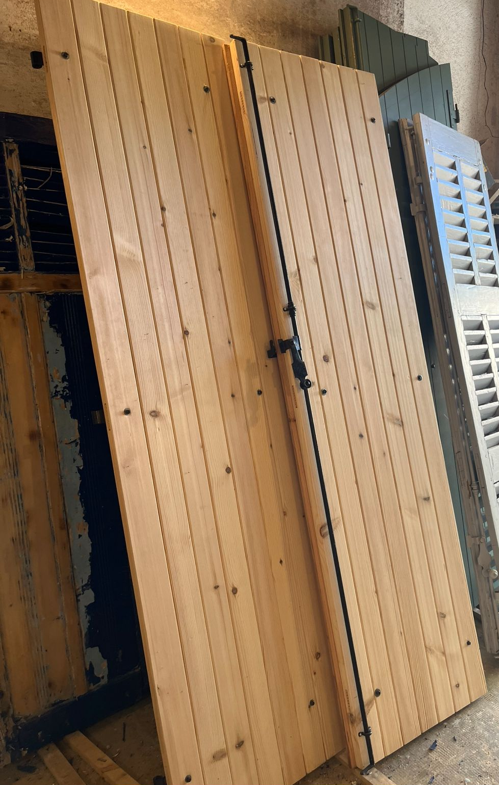 Deux volets en bois appuyés contre d'autres objets, comportant des lattes de bois verticales et un loquet central.