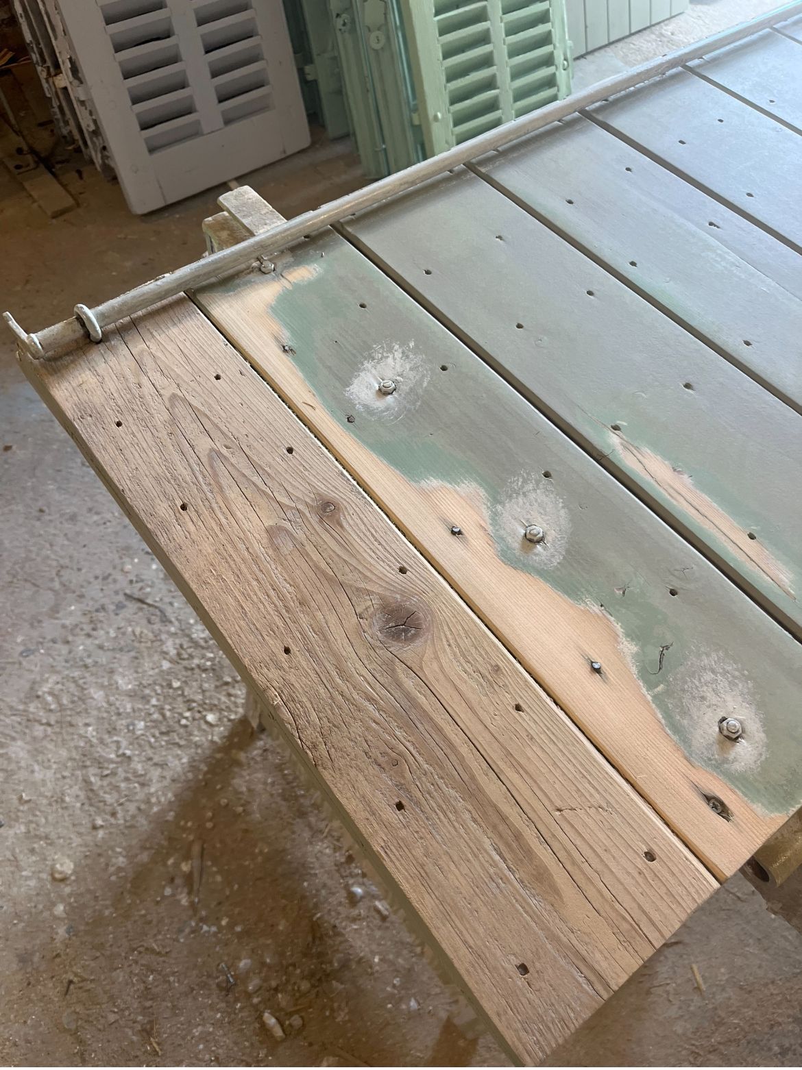 Volet en bois en cours de réparation à l'aide d'un serre-joint. Peinture vert clair et mastic à bois visibles.