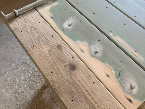 Plateau de table en bois, avec des parties peintes en vert et d'autres en bois brut, laissant apparaître des boulons et des trous.