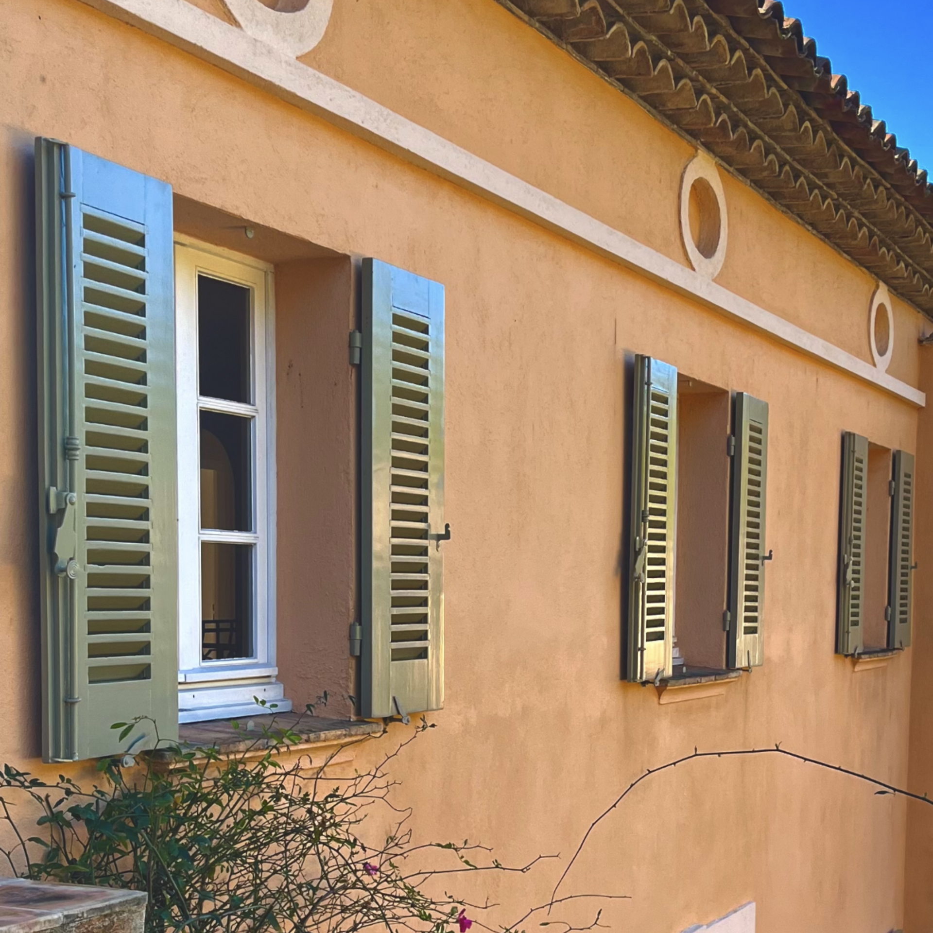 Bâtiment couleur pêche avec des volets verts aux fenêtres ; journée ensoleillée.