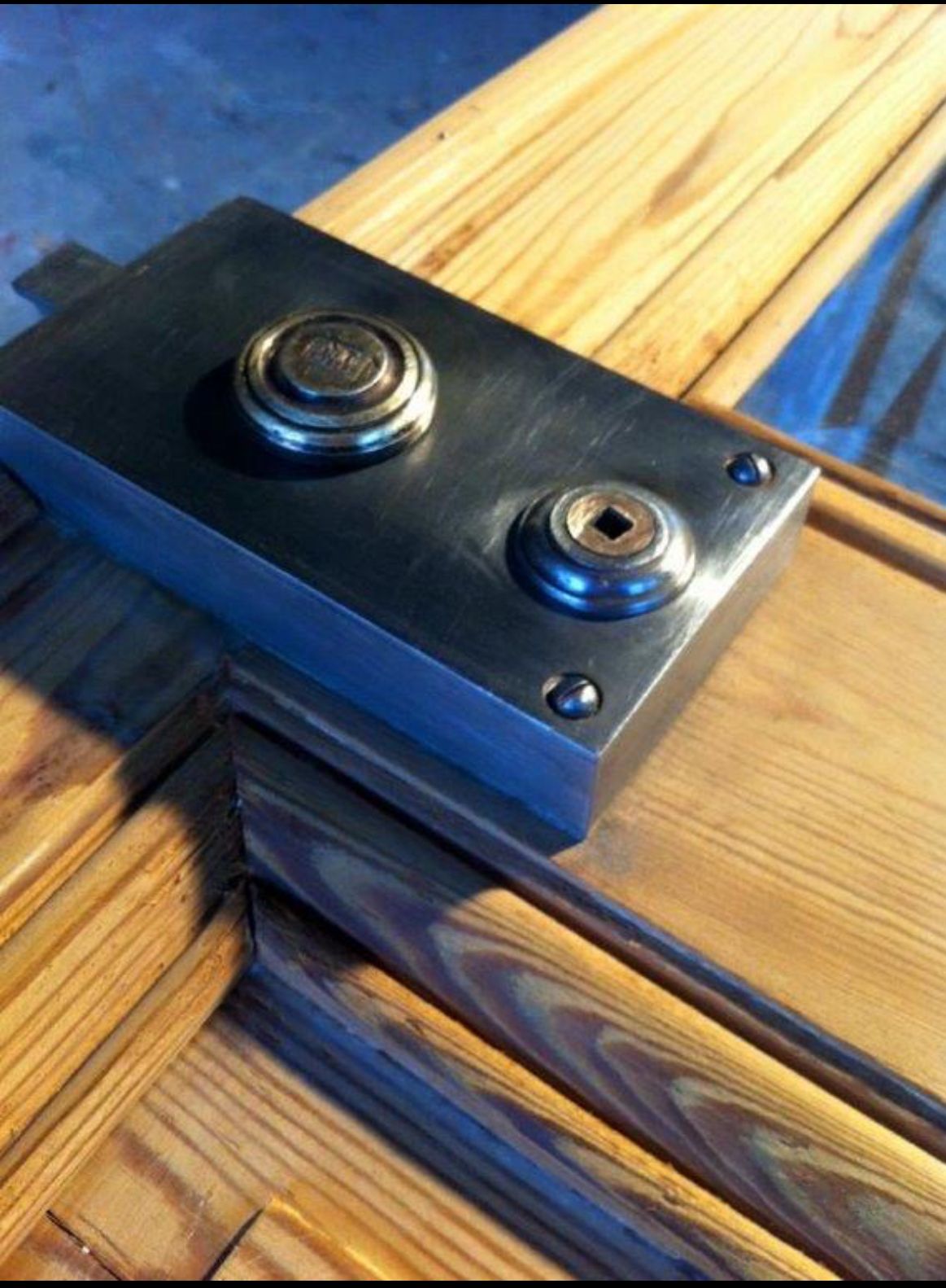 Gros plan sur une grande serrure métallique fixée sur une porte en bois. La serrure possède deux trous de clé circulaires.