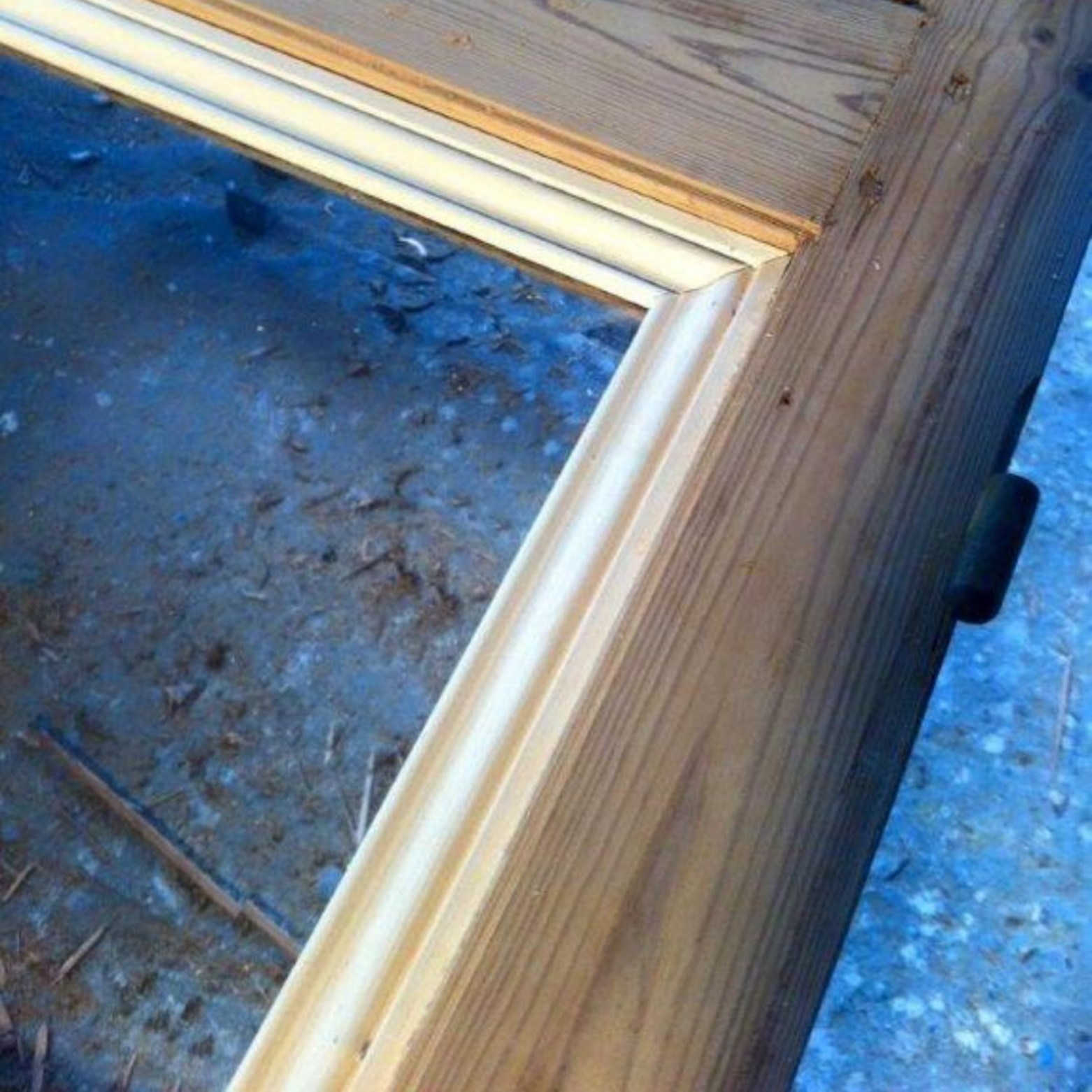 Détail d'un cadre de porte en bois, montrant une moulure en angle et une porte partiellement ouverte.