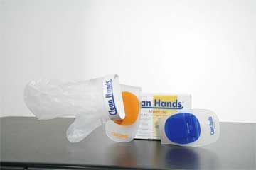 Auf einem Tisch liegt ein Plastikhandschuh neben einer Packung Händedesinfektionsmittel.