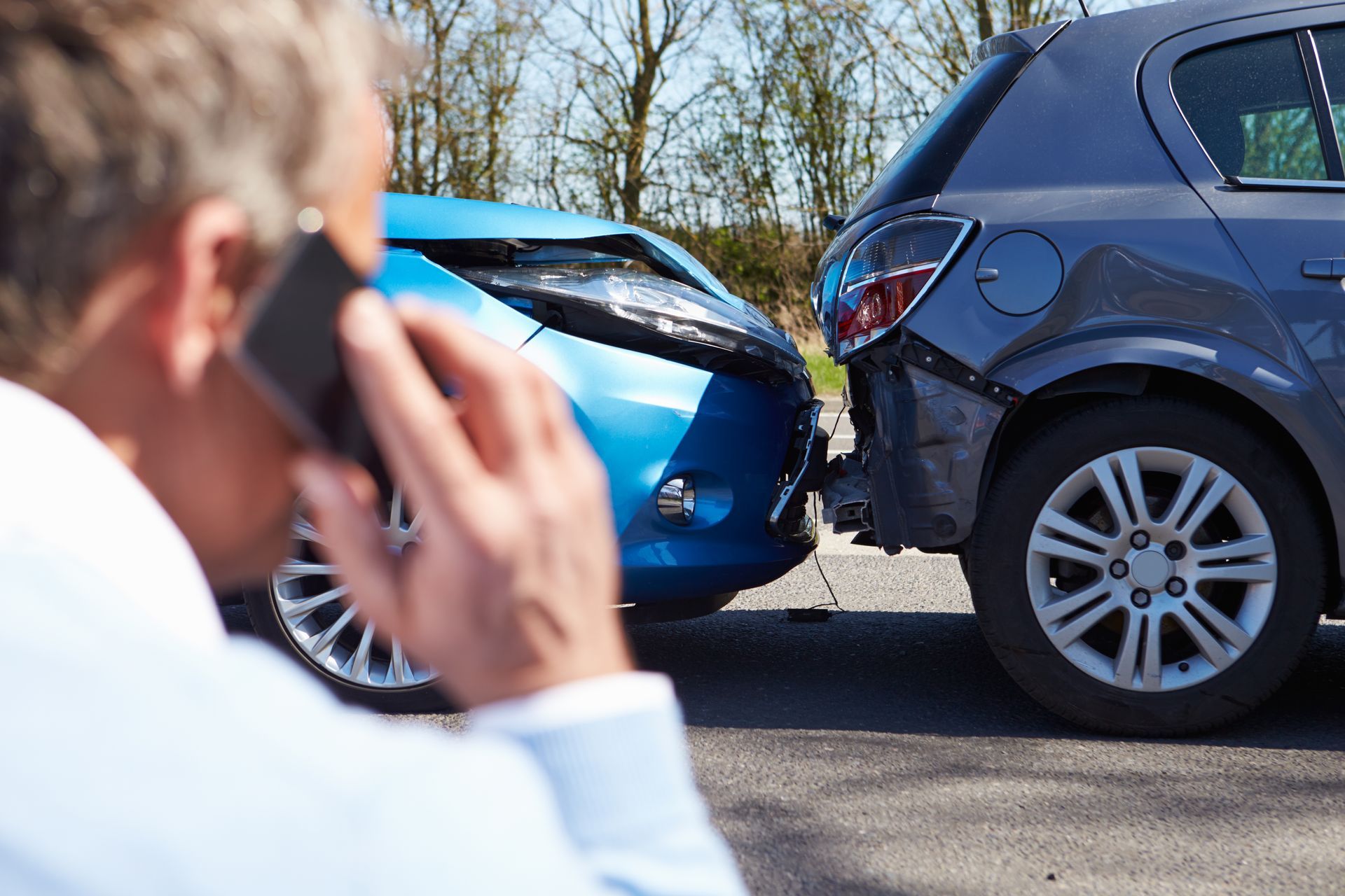 Hombre habla por teléfono después de un accidente automovilístico; autos azules y grises dañados en la calle.