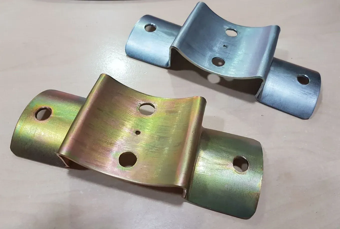 Dos soportes de metal doblados; uno de oro amarillo, otro de plata; ambos con orificios para montaje.