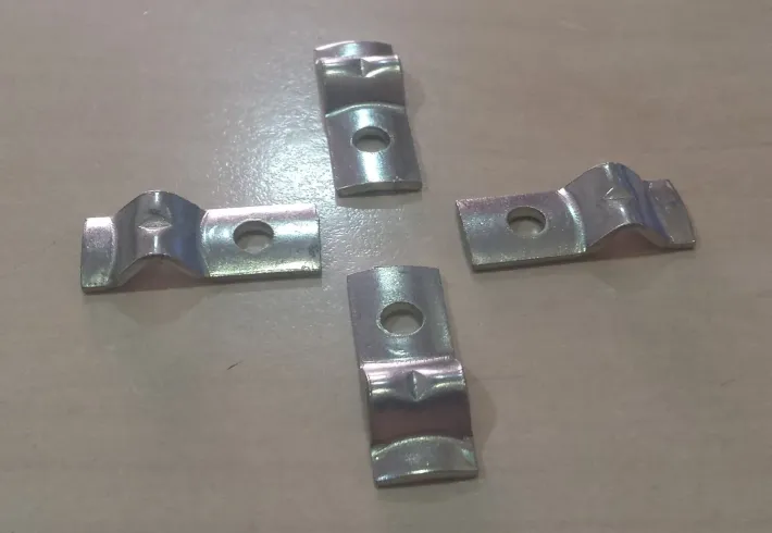 Cuatro soportes de metal plateado con agujeros centrales y puntas curvadas sobre una superficie de color marrón claro.