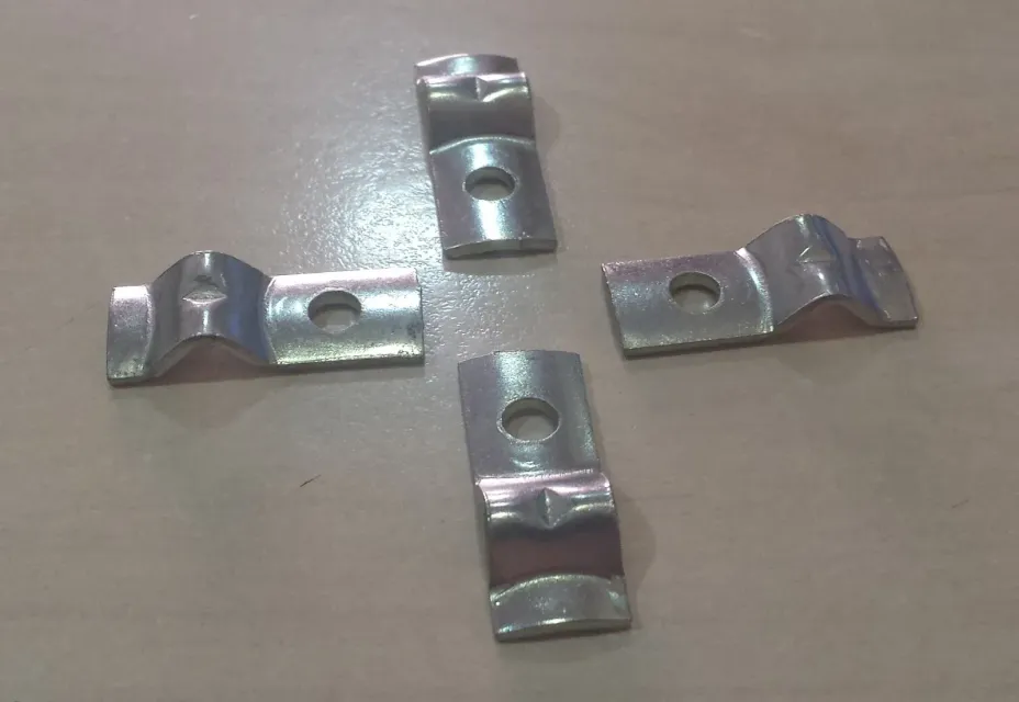 Cuatro soportes de metal plateado con agujeros centrales y puntas curvadas sobre una superficie de color marrón claro.