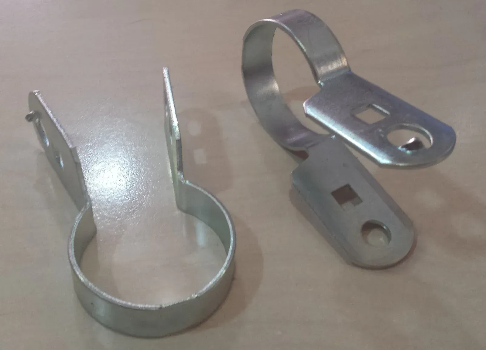 Dos clips para postes de cerca de metal galvanizado, cada uno con una banda circular y un extremo plano con agujeros.